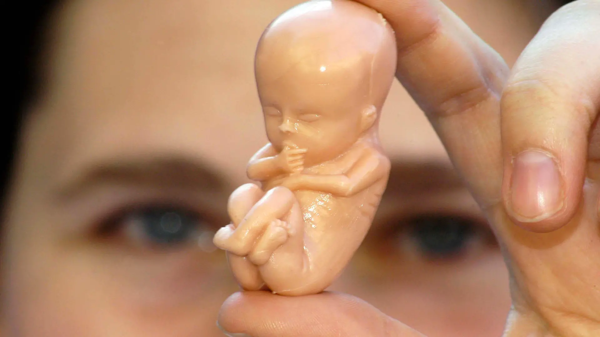 woman holding a small human embryo figure between her fingers