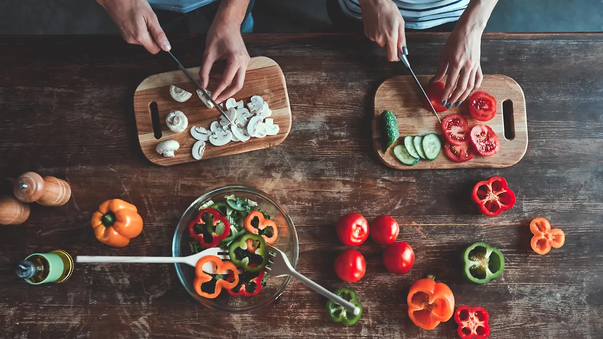 Cropped image of romantic couple is cooking on kitchen. Handsome man and attractive young woman are having fun together while making salad. Healthy lifestyle concept.