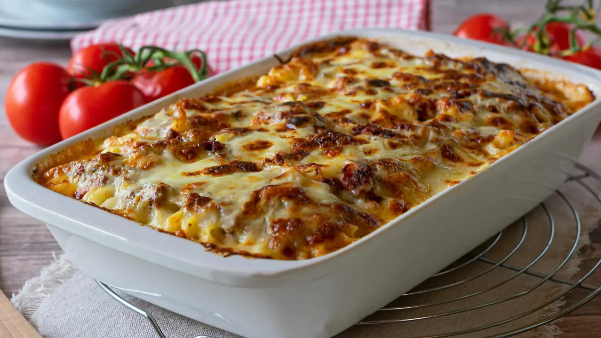 Delicious homemade italian gratin dish with home cooked bolognese sauce and bechamel sauce topped with mozzarella cheese and served in a white baking dish on rustic table background. Closeup view
