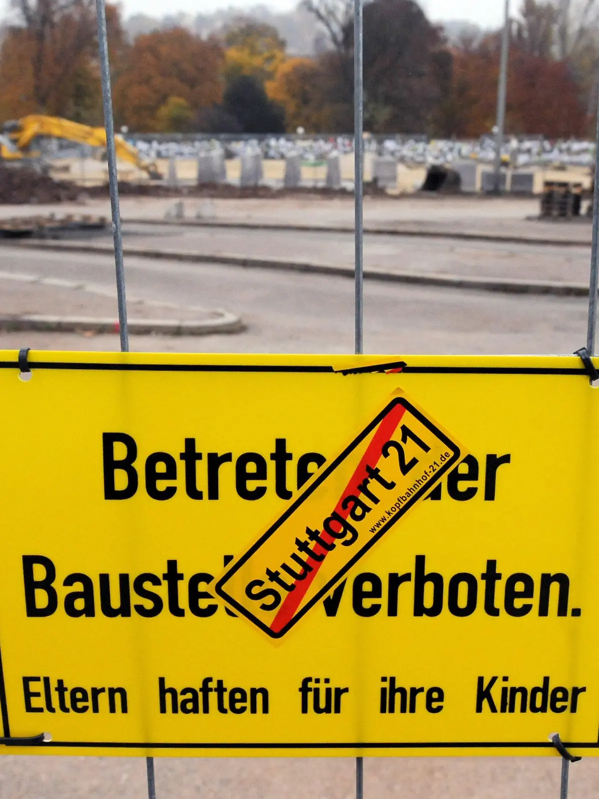 ARCHIV - Ein Aufkleber gegen das Bahnprojekt Stuttgart 21 klebt am 02.11.2010 in Stuttgart (Baden-Württemberg) an einem Schild, das an einem Bauzaun befestigt ist, im Hintergrund ist der ehemalige Omnibusbahnhof, auf dem Bauarbeiten am Grundwassermanagement für Stuttgart 21 stattfinden, zu sehen. Am 12.12.2012 tagt der Aufsichtsrat der Deutschen Bahn in Berlin. Auf der Tagesordung stehen die eventuellen Mehrkosten des mit 4,5 Milliarden Euro veranschlagten Bauprojekts. Foto: Marijan Murat/dpa  +++(c) dpa - Bildfunk+++