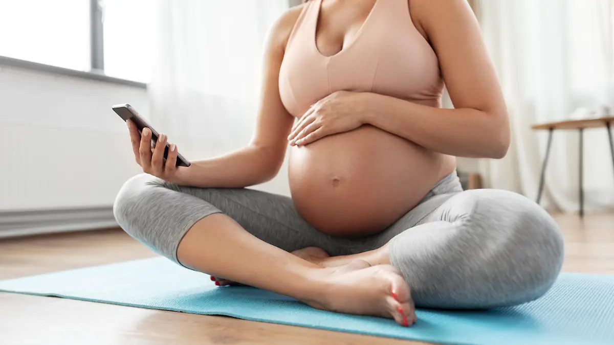 sport and people concept - happy pregnant woman with smartphone doing yoga at home