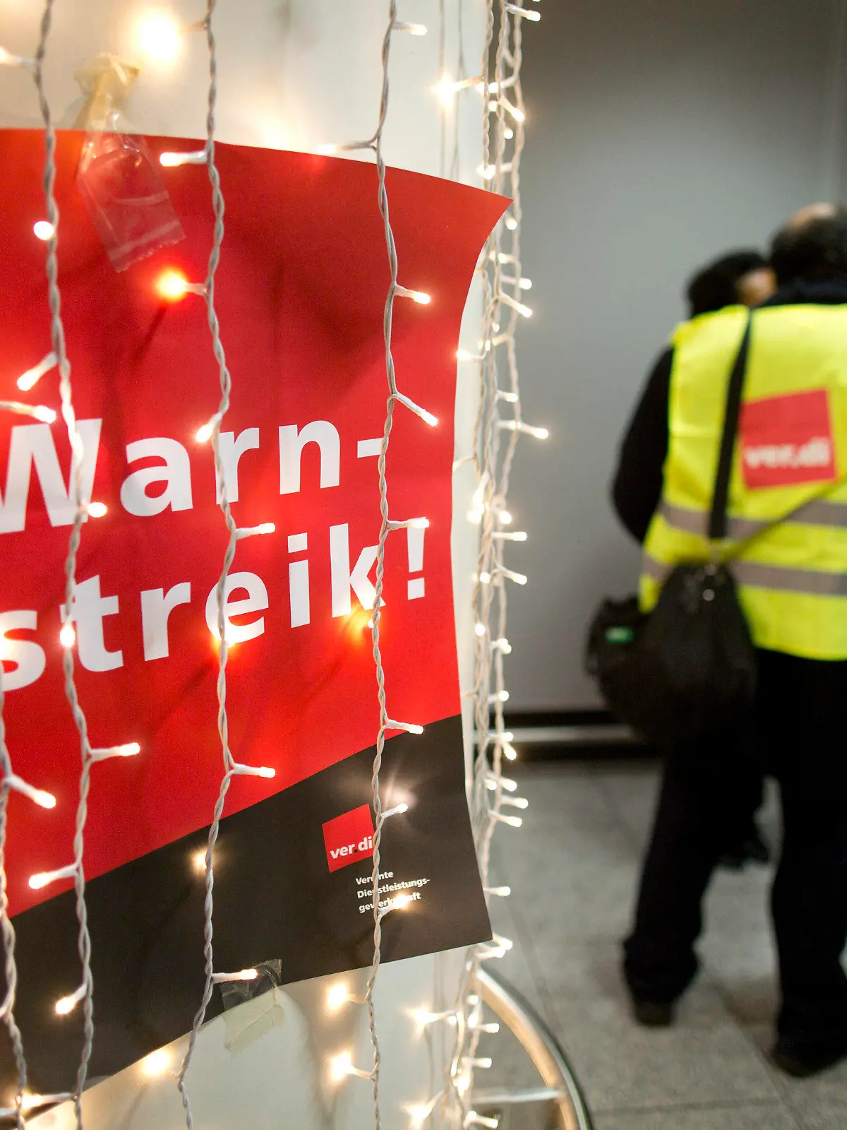 Ein Aufruf zum Warnstreik der Gewerkschaft Verdi hängt am 10.12.2012 am Flughafen von Frankfurt am Main (Hessen) hinter einer Weihnachtsbeleuchtung. Mehrere hundert Mitarbeiter des Sicherheitspersonals haben am frühen Montagmorgen an deutschen Flughäfen vorübergehend ihre Arbeit niedergelegt. In Verhandlungen macht sich die Gewerkschaft derzeit für geregelte Dienstpläne, unbefristete Arbeitsplätze und gerechte Löhne stark. Foto: Frank Rumpenhorst/dpa  +++(c) dpa - Bildfunk+++