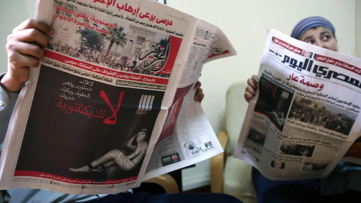 epa03495004 Unidentified Egyptian people read Al-Tahrir (L) and Masr el Youm independent newspapers, a front page (L) shows a black poster of a human covered in newspaper pages, chained in a celll, an inscription reading in Arabic 'a constitution that cancels rights and chains freedoms. No to dictatorship', in Cairo Egypt, 03 December 2012. Several independent and opposition Egyptian newspapers will suspend publication on 04 December to protest what they described as President Mohammed Morsi's 'dictatorship', as demonstrations against Morsi's rule continue to spread on 03 December. EPA/ANDRE PAIN  +++(c) dpa - Bildfunk+++