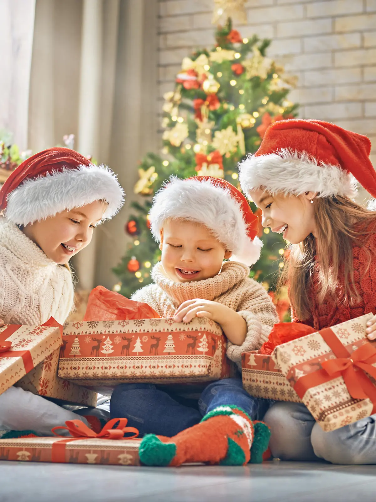 Merry Christmas and Happy Holidays! Cheerful cute children opening gifts. Kids having fun near tree in the morning. Loving family with presents in room.