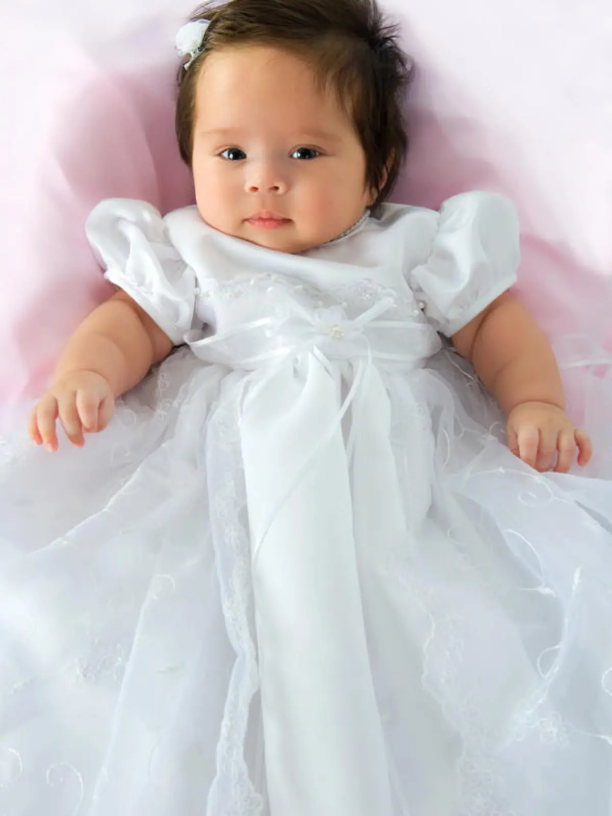 Newborn baby girl in a white baptism dress on a pink blanket