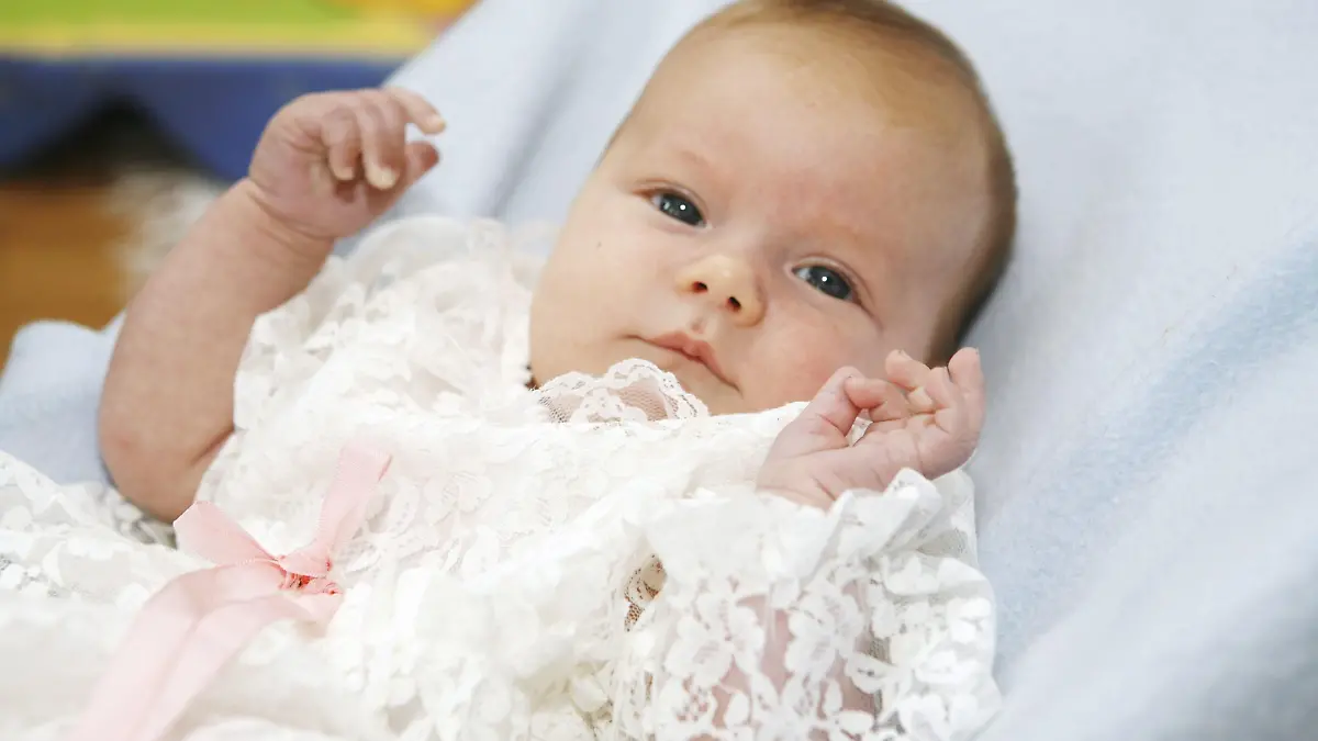 A 2-month-old baby girl dressed in a christening gown.