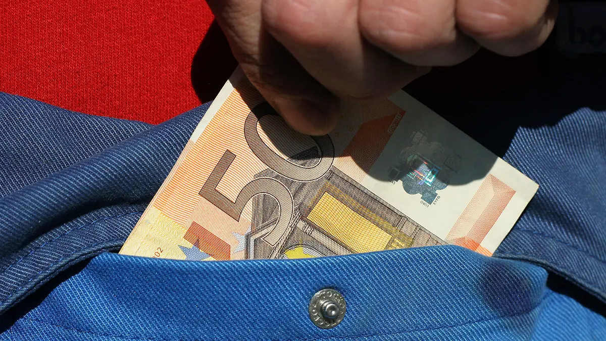Ein Handwerker steckt sich Bargeld in die Tasche seines Blaumanns (gestellte Aufnahme), aufgenommen am 21.09.2005 in Frankfurt am Main. Foto: Heiko Wolfraum +++(c) dpa - Report+++