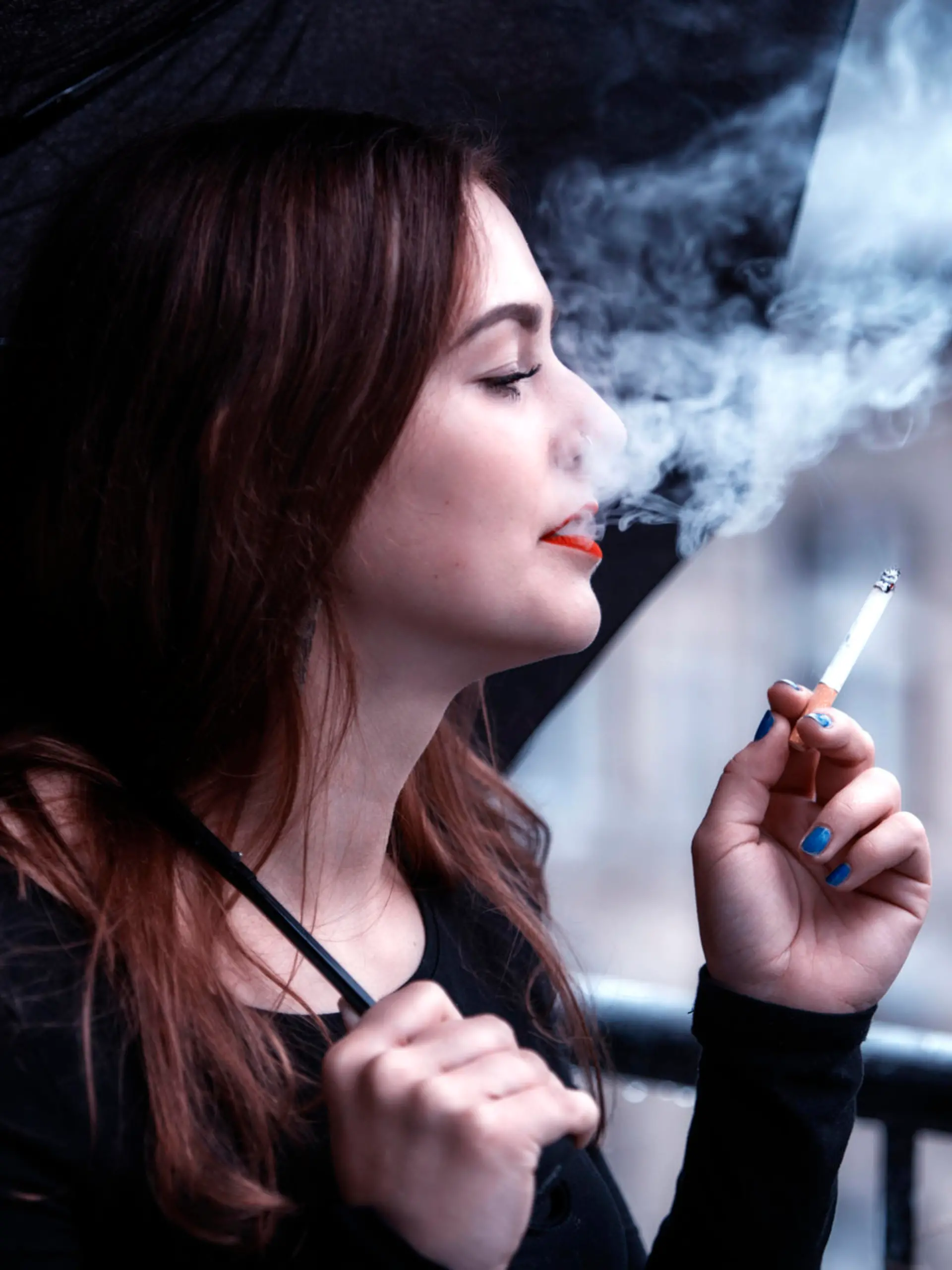 brunette young woman with umbrella in the rain smoking a cigarette