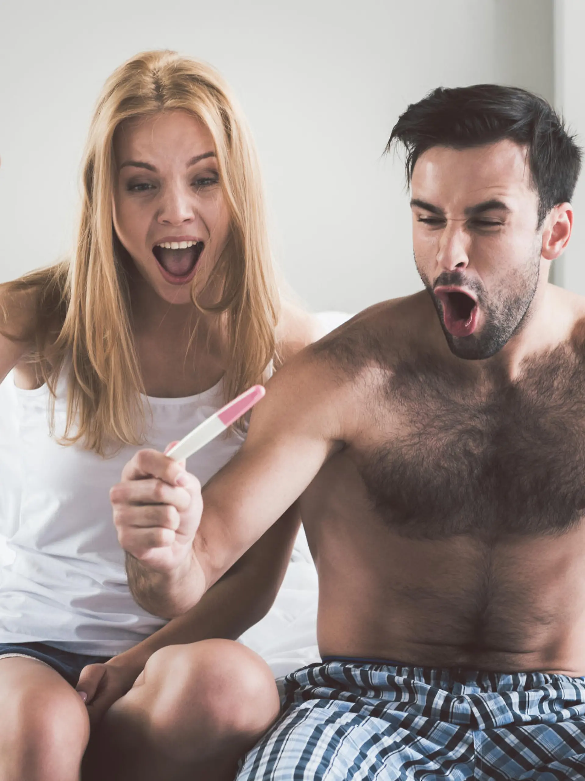 Frau und Mann schauen glücklich auf einen Schwangerschaftstest.