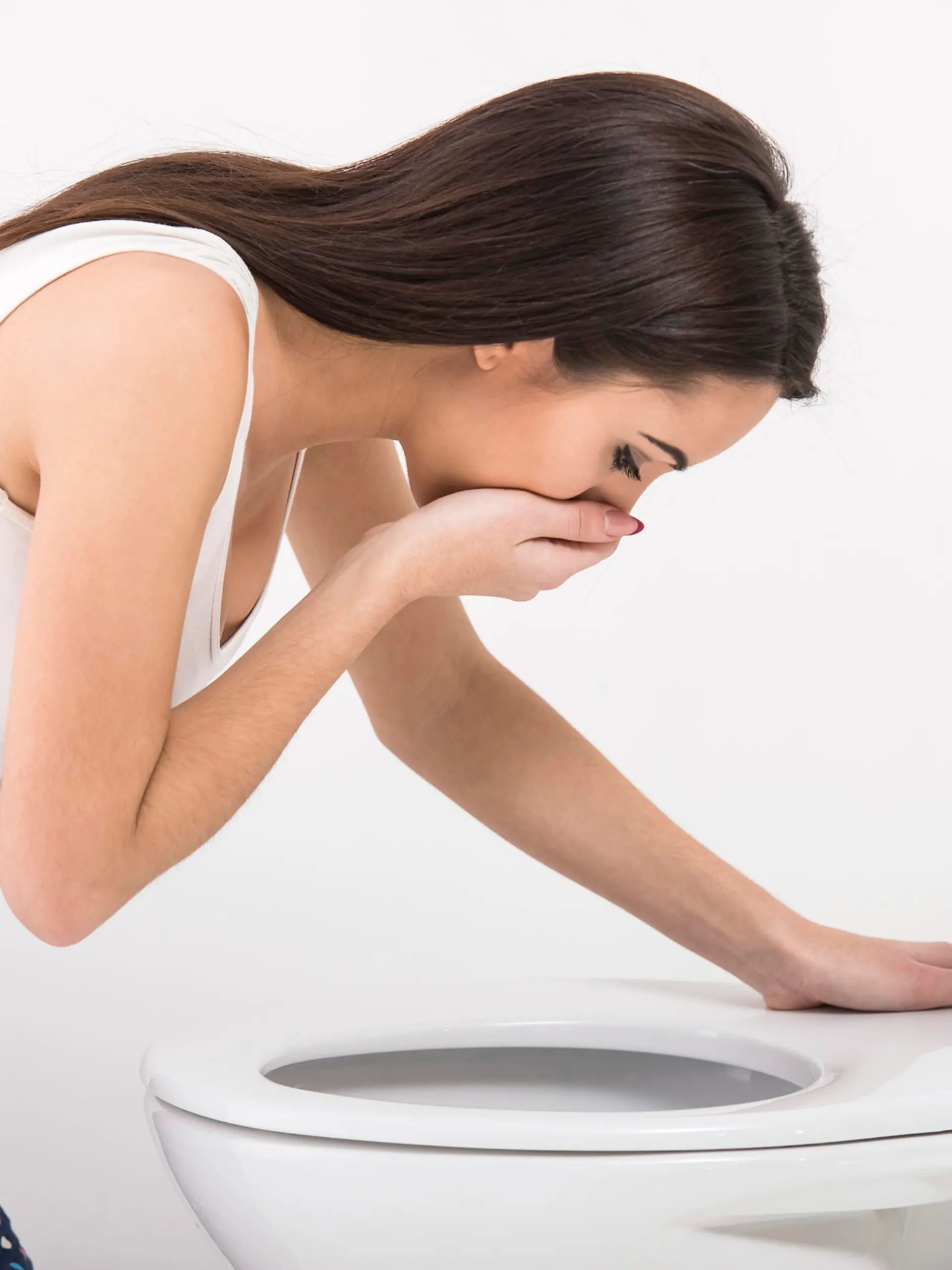 Young woman vomiting into the toilet bowl in the early stages of pregnancy or after a night of partying and drinking.Close-up of woman on toilet in morning.