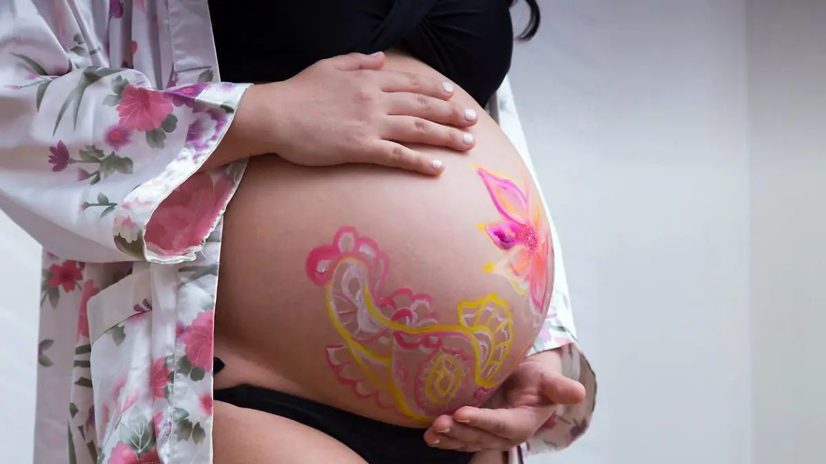 Closeup of a pregnant woman's belly with body art on it. Woman in a dressing gown carefully touches her painted tummy