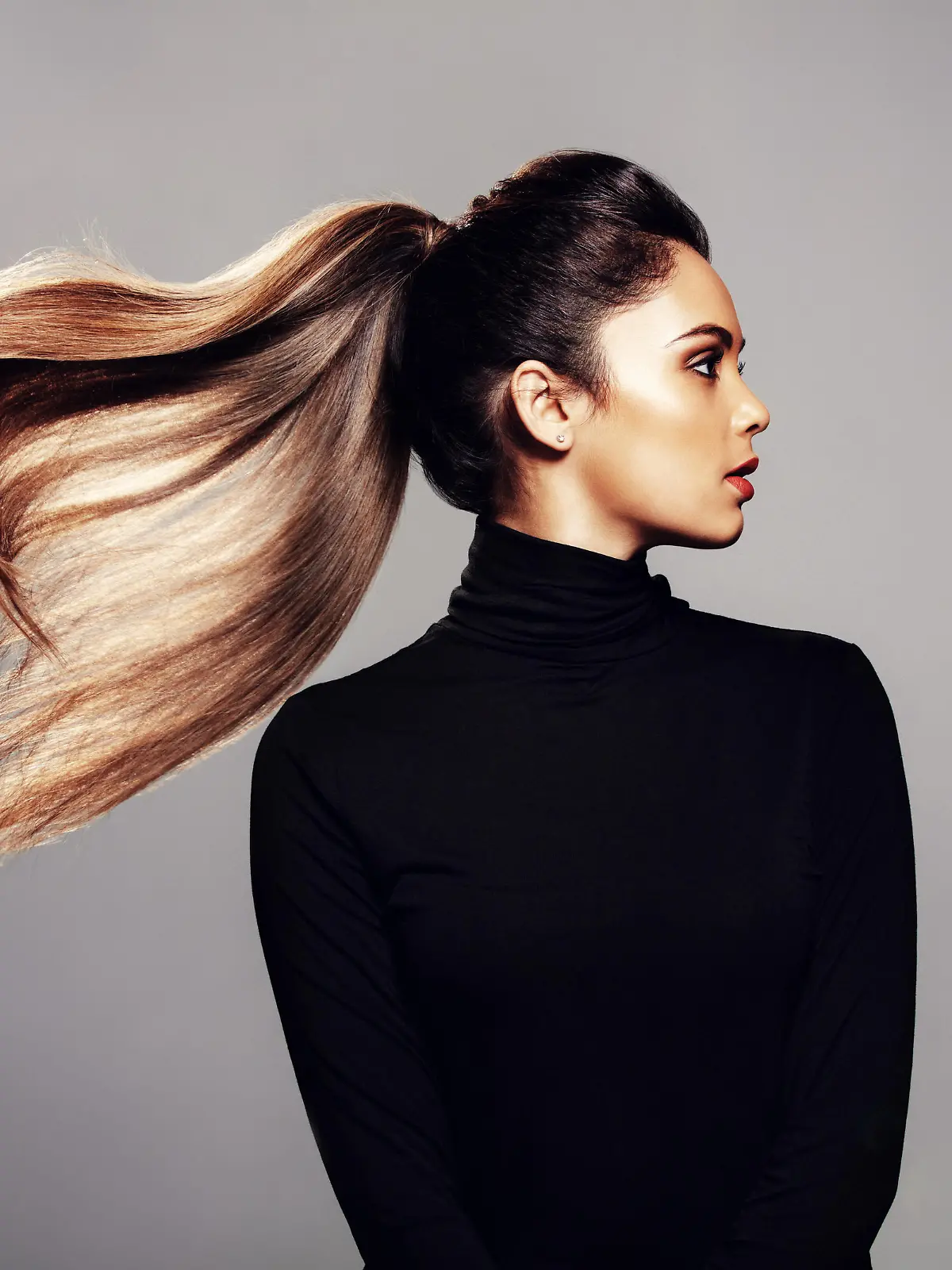 Studio shot of stylish young woman with flying hair against grey background. Female fashion model with long hair.