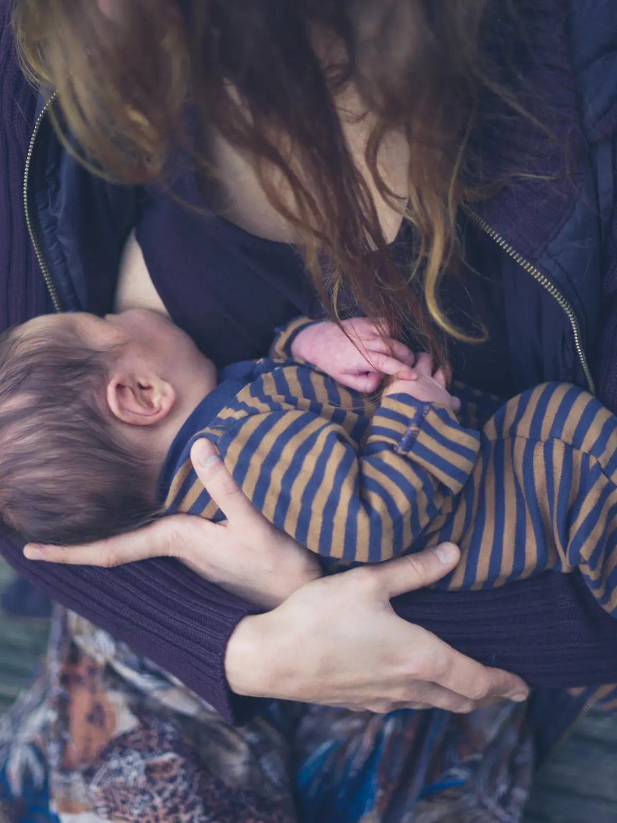 A young mother is breastfeeding her baby in a forest