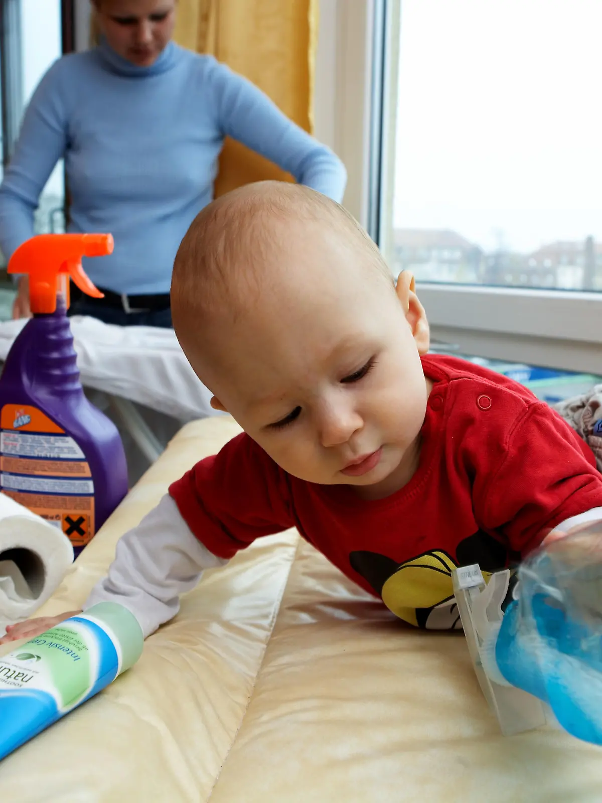 Während die Mutter mit Bügeln der Hausarbeit nach geht entdeckt ein Kleinkind seine Umwelt und greift nach einer Flasche mit Reinigungsmitteln, die um seinen Wickeltisch aufgestellt sind, aufgenommen in Leipzig am 01.12.2006 (gestelltes Illustrationsfoto zum Thema Gefahr im Haushalt für Kinder) Foto: Jörg Lange +++(c) dpa - Report+++