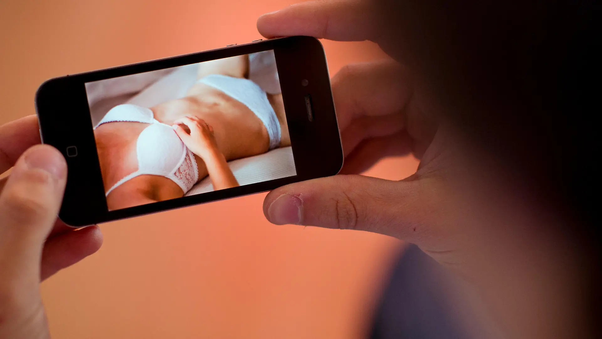 ILLUSTRATION - Ein junger Mann hält am 31.10.2013 in Hannover (Niedersachsen) ein Smartphone, auf dem ein erotisches Foto einer jungen erwachsenen Frau zu sehen ist. Zahlreiche Schulleiter aus Cloppenburg warnen in einem gemeinsamen Elternbrief vor dem neuen Trend «Sexting». Dabei versenden Jugendliche erotische Fotos oder Nacktbilder von sich per Smartphone an Freunde oder laden sie in sozialen Netzwerken hoch. Foto: Julian Stratenschulte/dpa