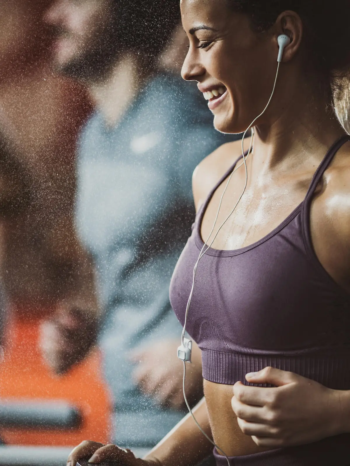 Eine glücklich aussehende Frau trainiert auf dem Laufband im Fitnessstudio. Über Kopfhörer hört sie Musik auf ihrem Handy.