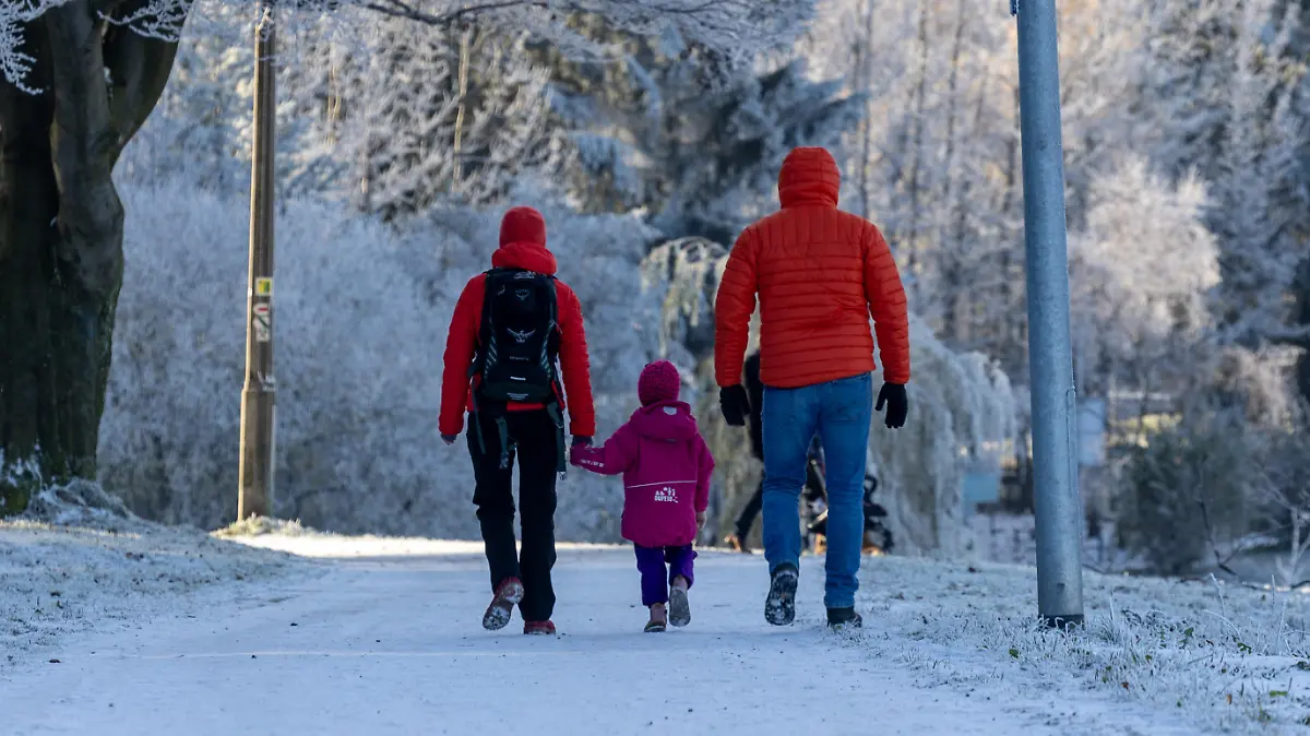 Menschen gehen auf einen verschneiten Weg spazieren. Im Erzgebirge gingen zwei bis drei Zentimeter Neuschnee nieder.