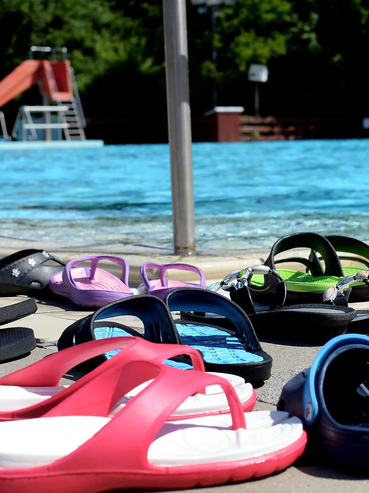ARCHIV - Bunte Badeschuhe stehen am 05.06.2015 an einem Beckenrand im Freibad Bokeloh in der Ortschaft Bokeloh nahe Hannover (Niedersachsen). Foto: Susann Prautsch/dpa (zu dpa Korr-Bericht "Was anziehen bei 40 Grad? - Wenn Trekkingsandale und Strohhut kommen" vom 03.07.2015) +++(c) dpa - Bildfunk+++