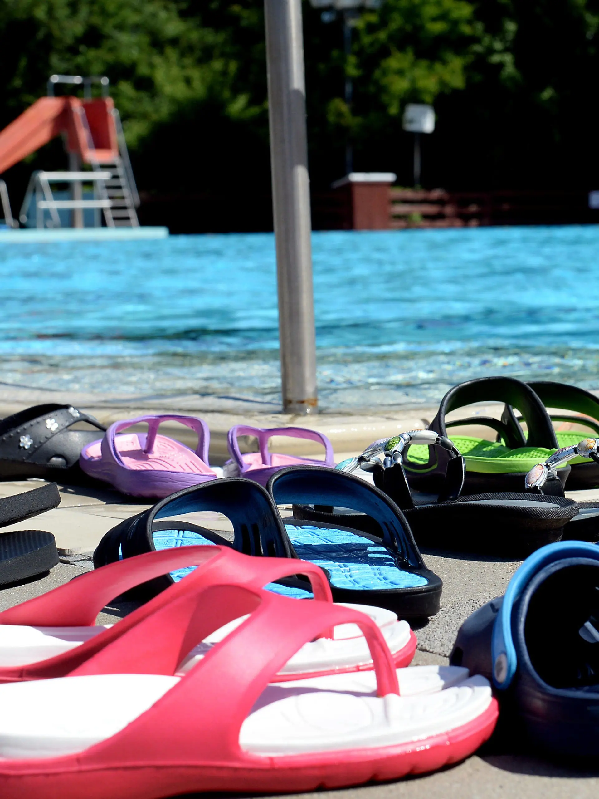 ARCHIV - Bunte Badeschuhe stehen am 05.06.2015 an einem Beckenrand im Freibad Bokeloh in der Ortschaft Bokeloh nahe Hannover (Niedersachsen). Foto: Susann Prautsch/dpa (zu dpa Korr-Bericht "Was anziehen bei 40 Grad? - Wenn Trekkingsandale und Strohhut kommen" vom 03.07.2015) +++(c) dpa - Bildfunk+++