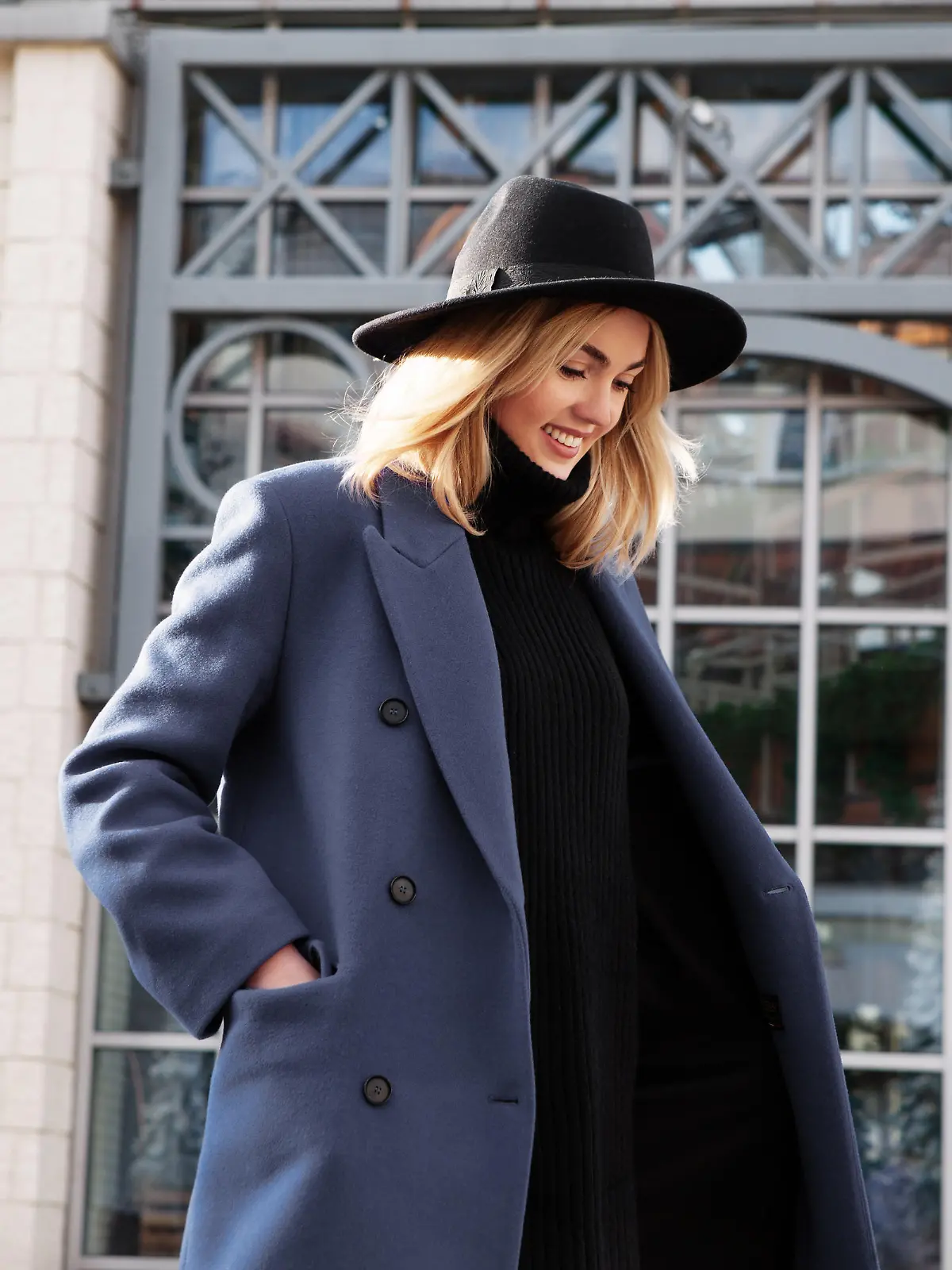 Lifestyle portrait of fashionable woman wearing winter or spring outfit, felt hat, gray wool coat, turtleneck. Outdoors. Female stylish Model smiling, walking city Street. Street fashion trend