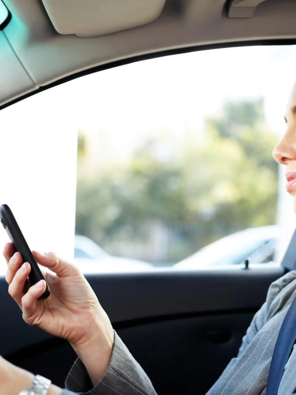 Frau schaut während des Autofahrens auf ihr Handy.