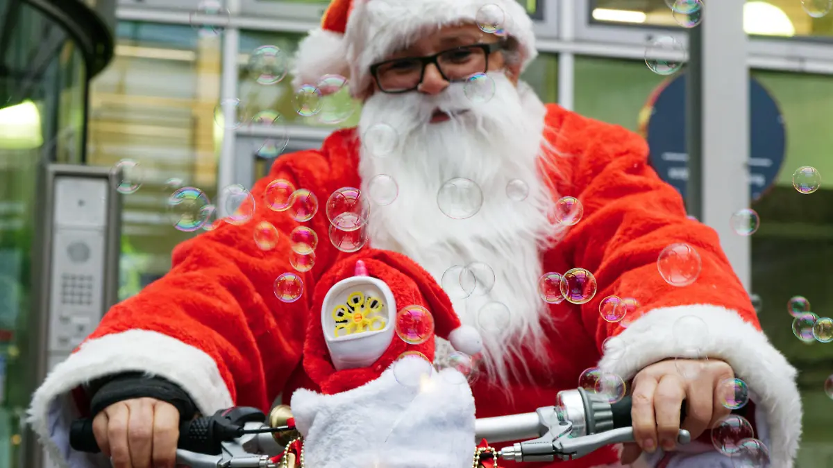 04.12.2022, Nordrhein-Westfalen, Köln: Eine als Nikolaus verkleidete Radfahrerin lässt bei einer Flashmob-Aktion der Kölner Verkehrsbetriebe (KVB) Seifenblasen aus einer am Fahrrad montierten Maschine aufsteigen. Mit einem Flashmob wollen die Kölner Verkehrsbetriebe auf die angespannte Lage der Branche aufmerksam machen. Deshalb rufen sie zum «KVB-Rad Nikolaus Flashmob» auf. Foto: Henning Kaiser/dpa +++ dpa-Bildfunk +++
