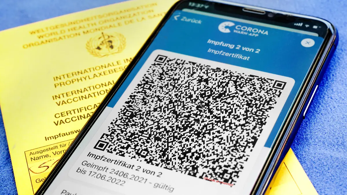  QR-Code, das digitale Impfzertifikat in der Corona Warn-App auf einem Smartphone bestätigt eine abgeschlossenen Impfung gegen Covid-19. Liegt auf der gelben Internationalen Impfbescheinigung, Impfpass. - ACHTUNG QR-Code und persönliche Angaben sind unkenntlich gemacht *** QR code, the digital vaccination certificate in the Corona Warn app on a smartphone confirms a completed vaccination against Covid 19 Lies on the yellow International Vaccination Certificate, Vaccination Card ATTENTION QR code and personal details are made unrecognizable
