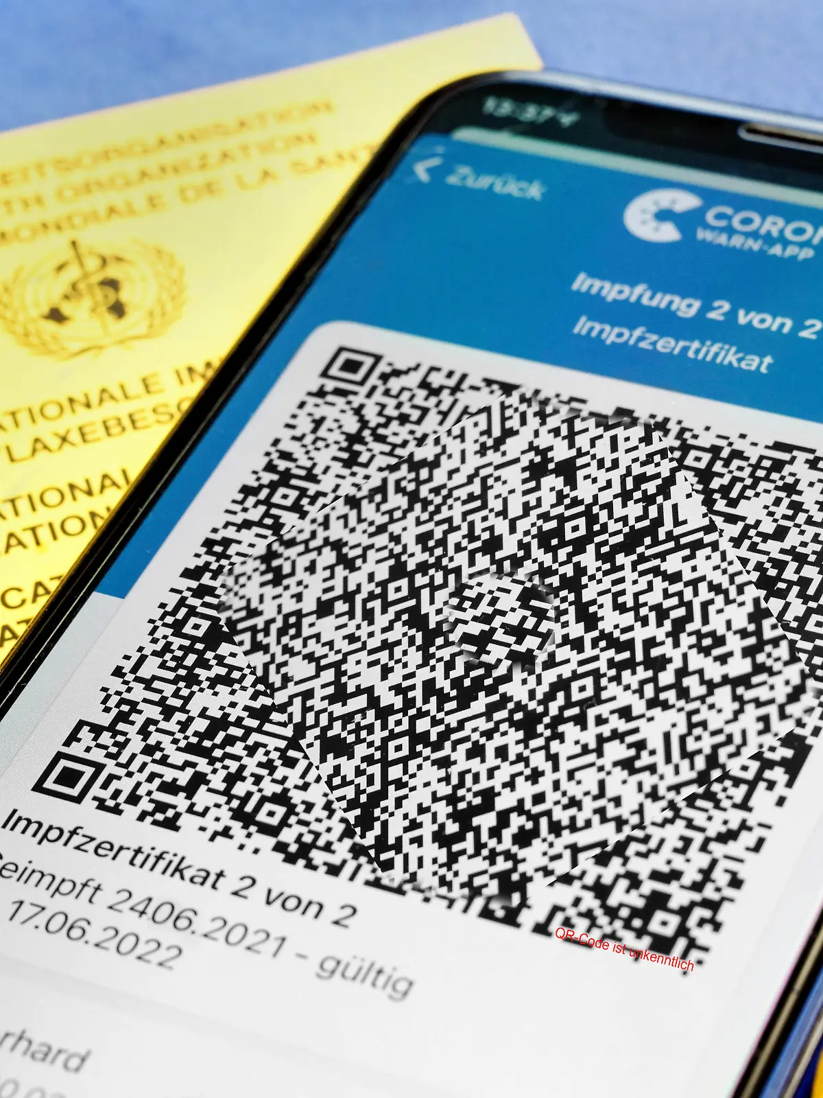  QR-Code, das digitale Impfzertifikat in der Corona Warn-App auf einem Smartphone bestätigt eine abgeschlossenen Impfung gegen Covid-19. Liegt auf der gelben Internationalen Impfbescheinigung, Impfpass. - ACHTUNG QR-Code und persönliche Angaben sind unkenntlich gemacht *** QR code, the digital vaccination certificate in the Corona Warn app on a smartphone confirms a completed vaccination against Covid 19 Lies on the yellow International Vaccination Certificate, Vaccination Card ATTENTION QR code and personal details are made unrecognizable