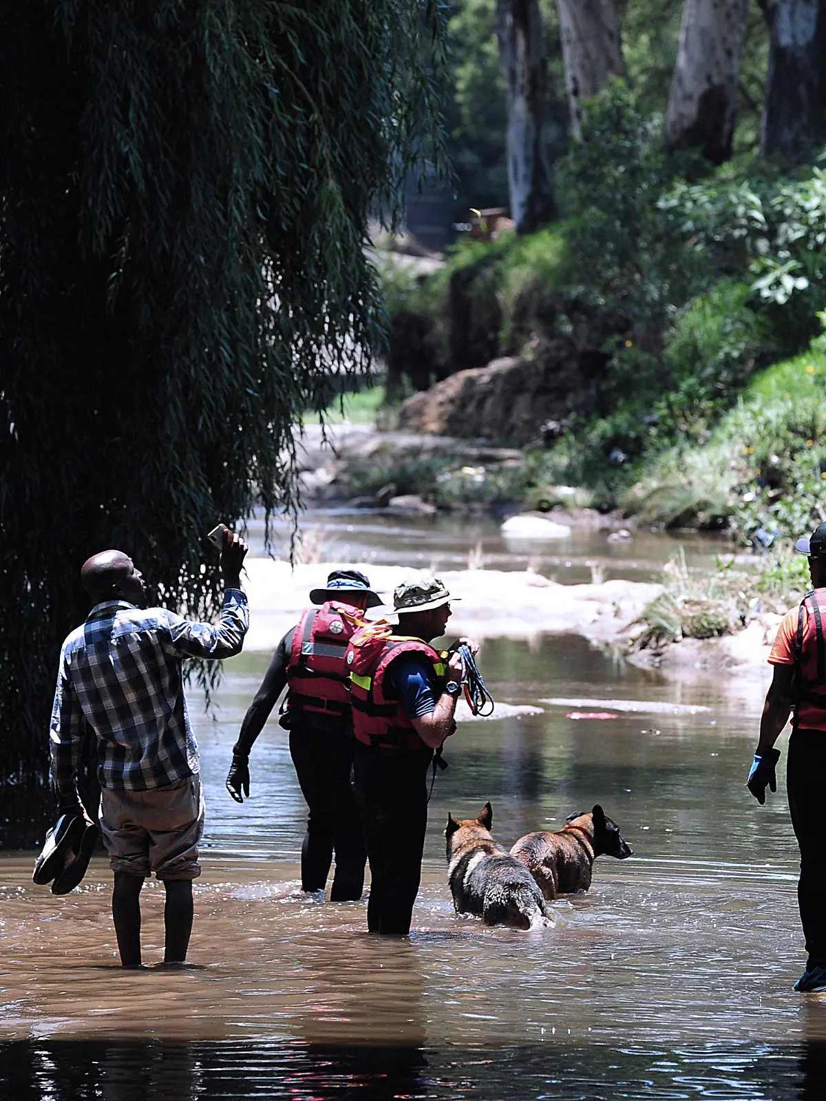 04.12.2022, Südafrika, Johannesburg: Rettungskräfte gehen mit ihren Hunden während der Rettungsarbeiten durch den Jukskei-Fluss. In einem Vorort der südafrikanischen Metropole Johannesburg sind mindestens neun Teilnehmer einer Taufzeremonie ertrunken. 33 Täuflinge, die sich am Samstag in Bramley Park am Ufer des Jukskei-Flusses versammelt hatten, seien von einer plötzlichen Sturzflut und starken Strömung überrascht worden, erklärte ein Sprecher der Rettungskräfte am Sonntag. Foto: -/AP/dpa +++ dpa-Bildfunk +++