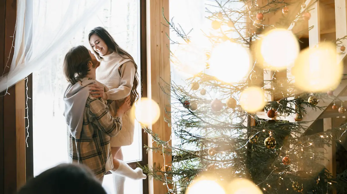 Hugging stylish love couple girl, guy lie on skin on floor in cozy wooden country house,chalet in winter forest.Celebrating new year eve.Gifts,family holiday.Romantic weekend.Decorated Christmas tree.