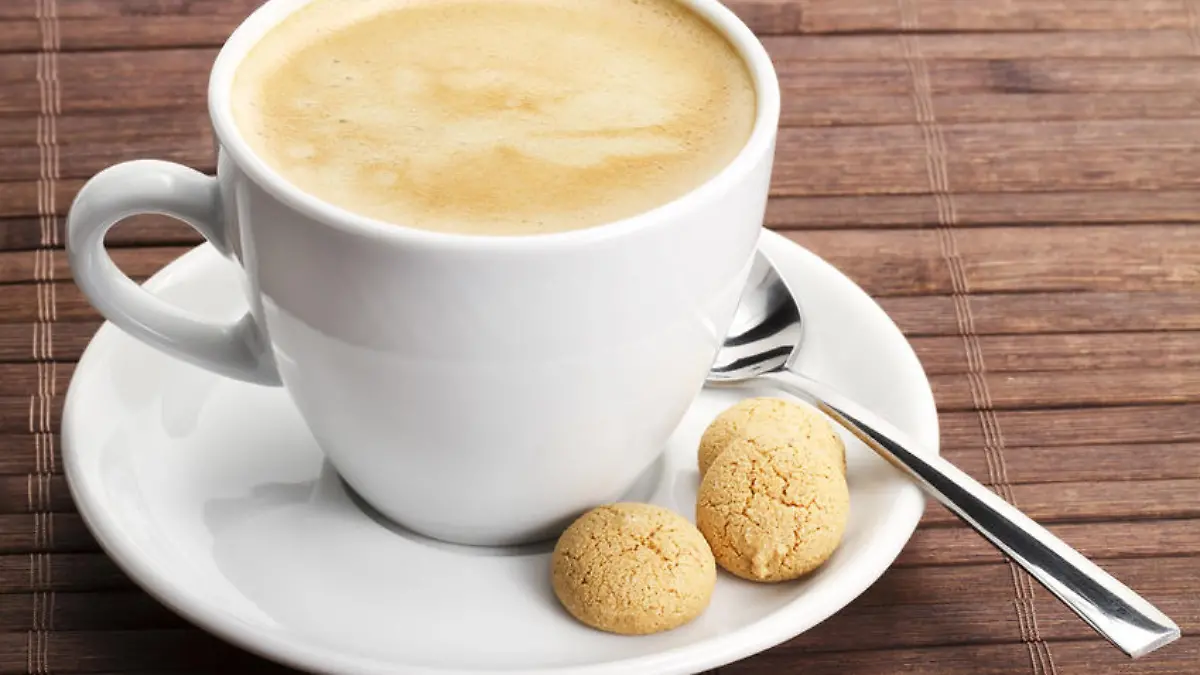 kaffee in einer weissen tasse mit einem lÃ¶ffel und amarettini auf hÃ¶lzernem hintergrund