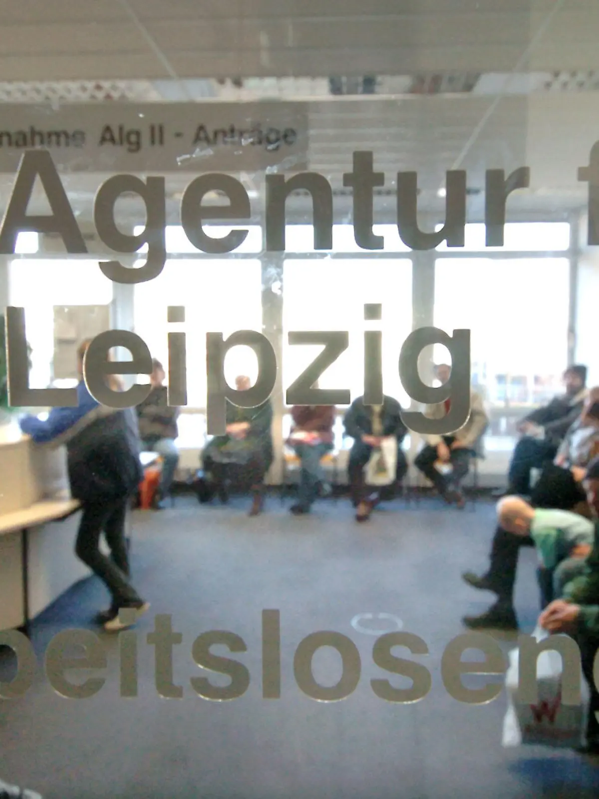 Hinter einer Glasscheibe einer Agentur für Arbeit in Leipzig herrscht am Dienstag (28.12.2004), dem offiziellen vorletzten Öffnungstag in diesem Jahr, noch großer Andrang bei der Antragsannahme für Arbeitslosengeld II. Im Bereich der Arbeitsagentur in Leipzig wurden in den letzten zwei Monaten rund 40.000 Bescheide an Antragsteller für ALG II herausgeschickt. Ab Januar 2005 erhalten in Deutschland Bezieher der bisherigen Arbeitslosenhilfe sowie arbeitsfähige Sozialhilfempfänger das neue Arbeitslosengeld II. Foto:Waltraud Grubitzsch/lsn +++(c) dpa - Bildfunk+++