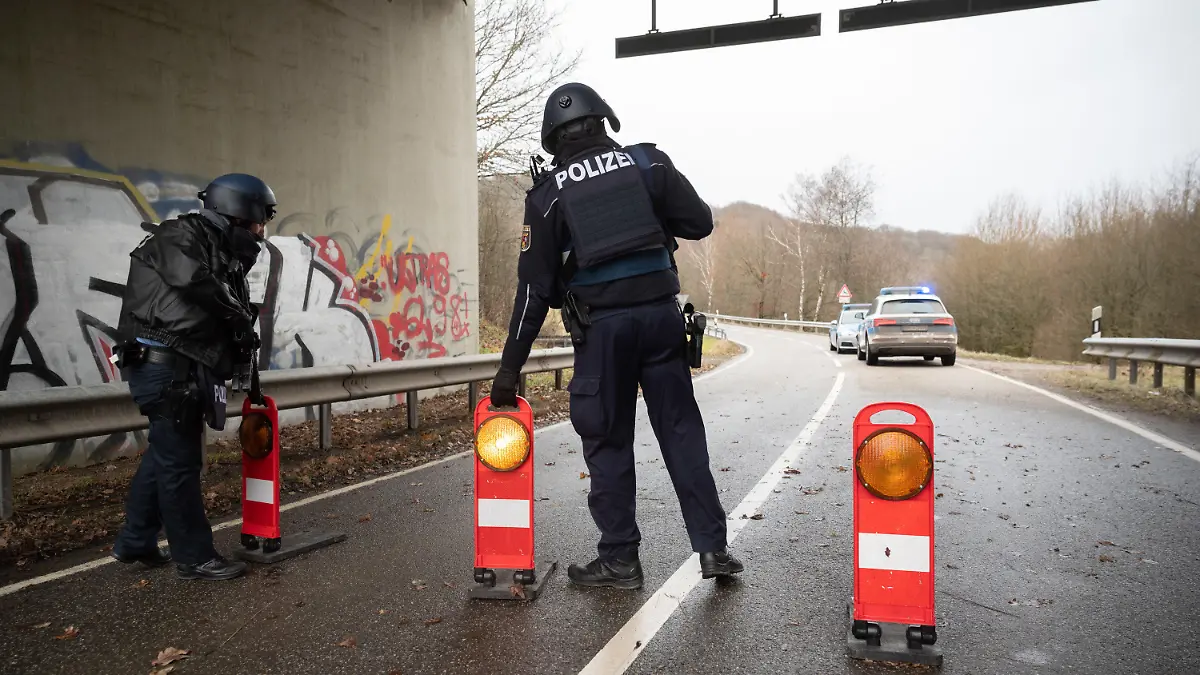 31.01.2022, Rheinland-Pfalz, Mayweilerhof: Polizeibeamte stehen an einer Absperrung an der Kreisstraße 22 rund einen Kilometer von dem Tatort, an dem zwei Polizeibeamte durch Schüsse getötet wurden. Foto: Sebastian Gollnow/dpa +++ dpa-Bildfunk +++