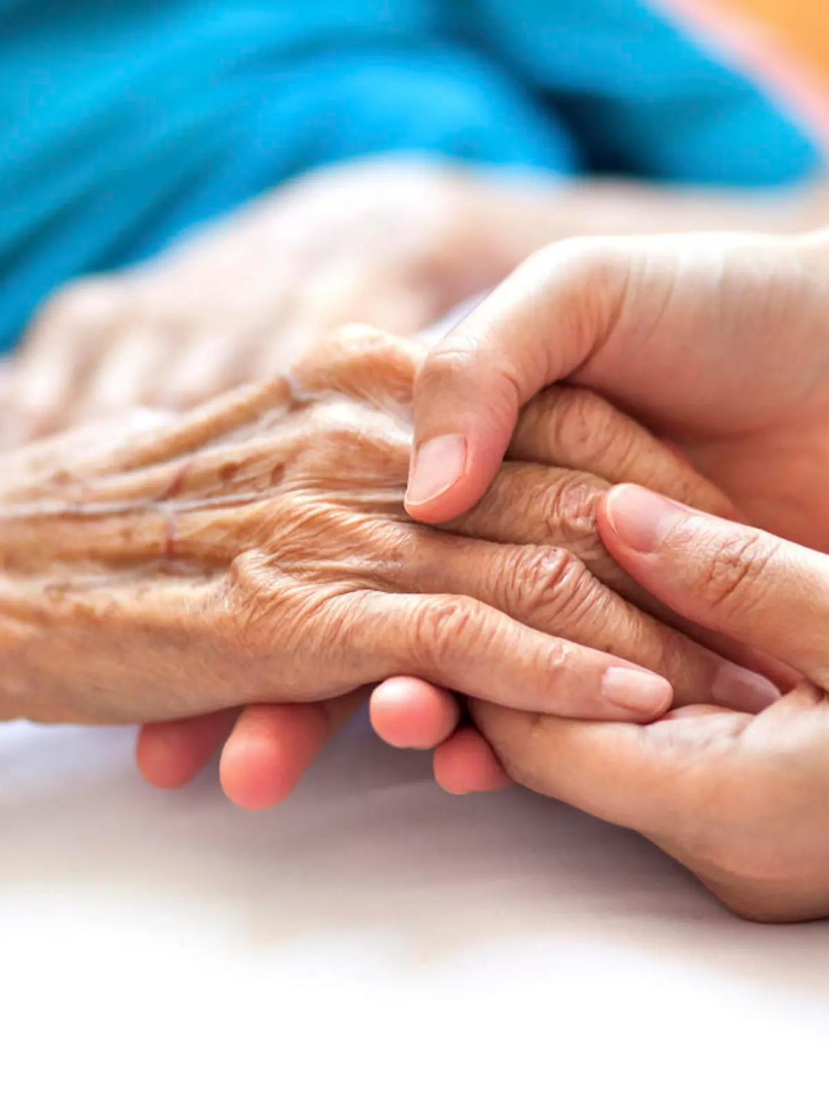 Woman holding senior woman's hand on bed
