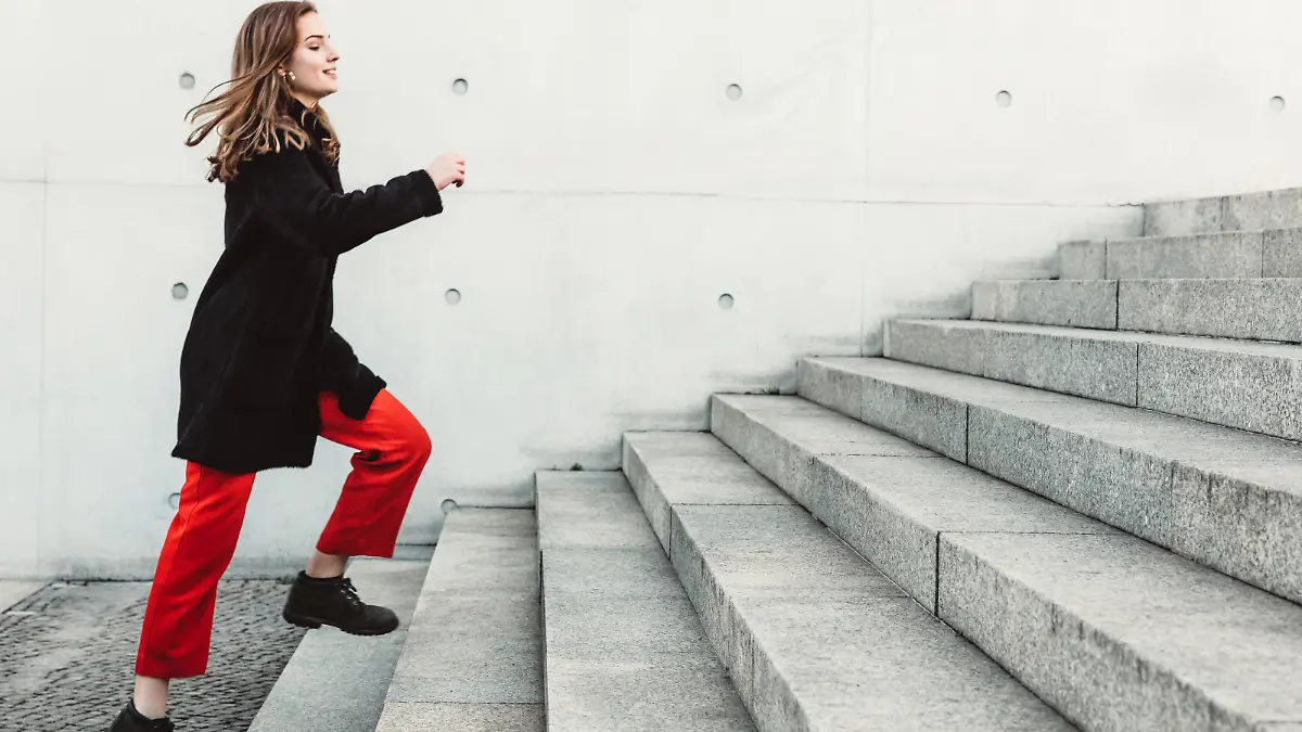 Eine Frau ist draußen und steht am Fuße einer größeren Treppe, die sie in kürze erklimmen wird.