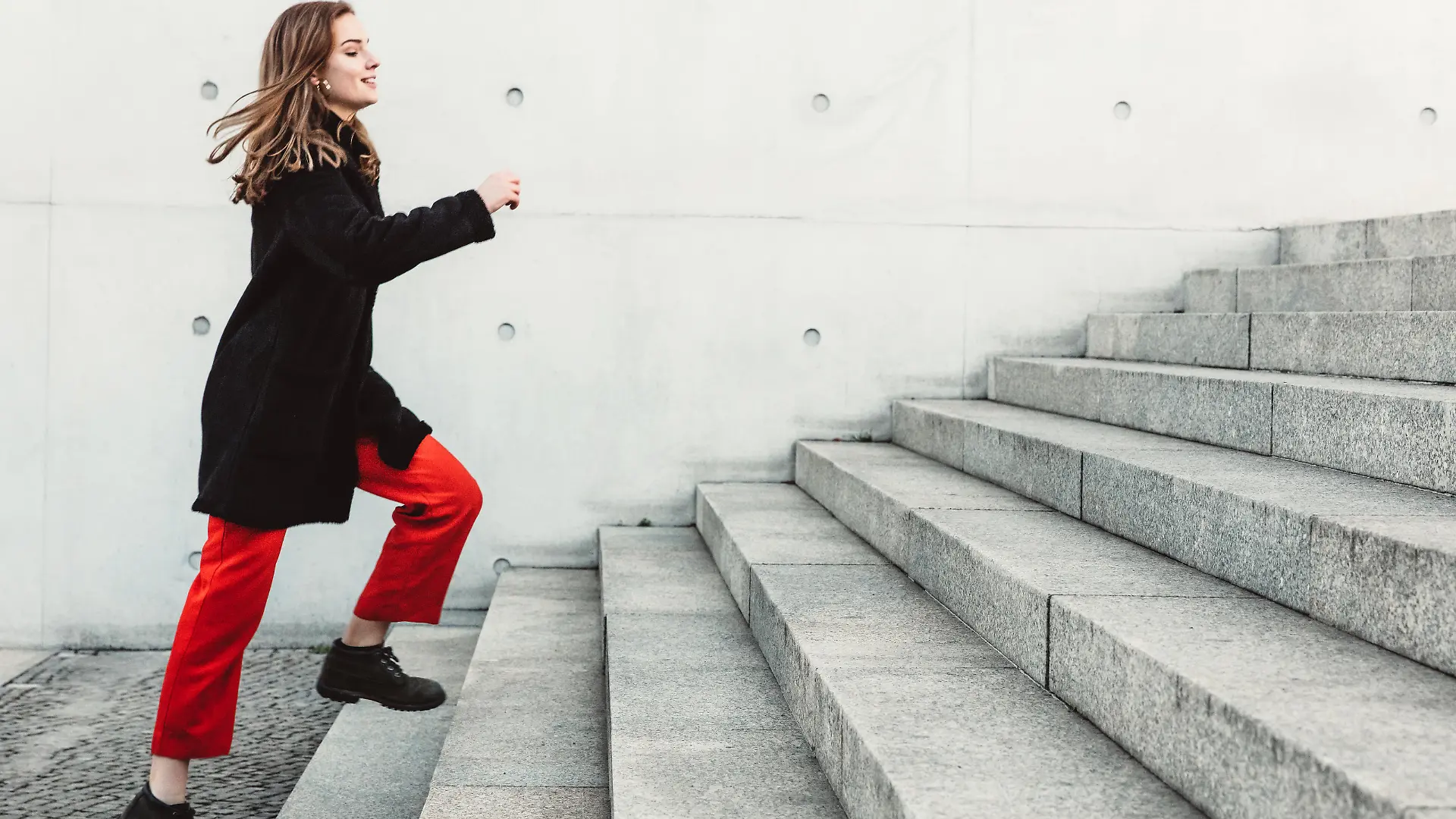 Eine Frau ist draußen und steht am Fuße einer größeren Treppe, die sie in kürze erklimmen wird.