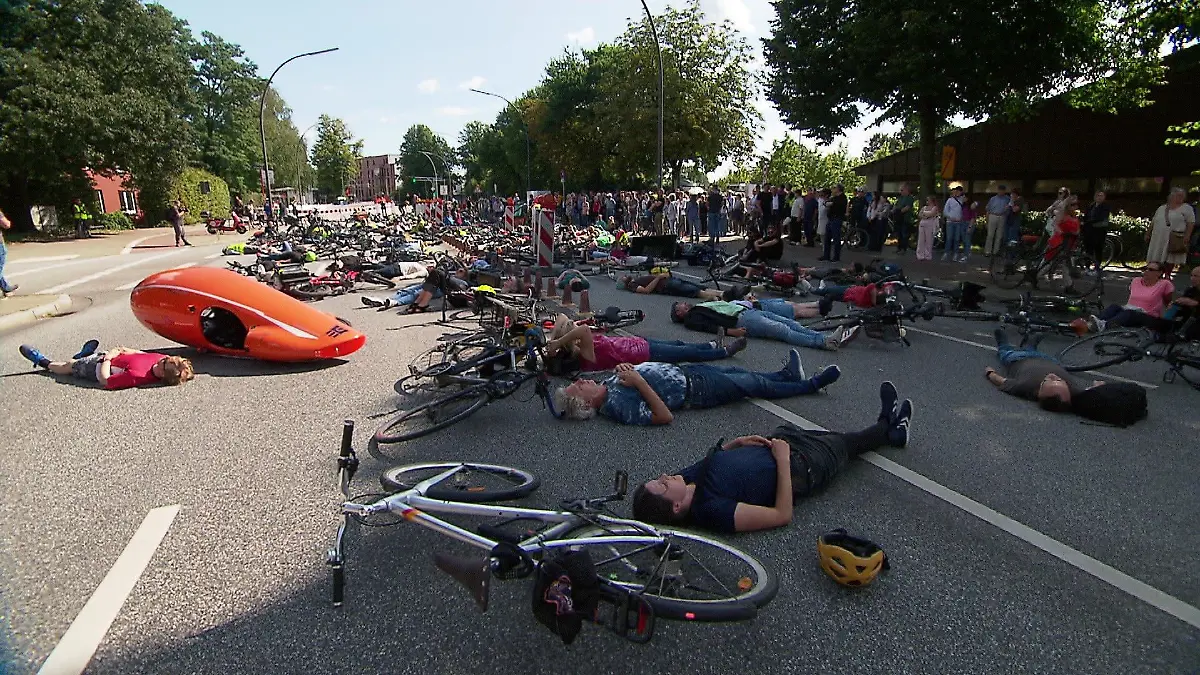 Auf einer abgesperrten Straße legen sich Menschen in einer Protestaktion auf die Straße.