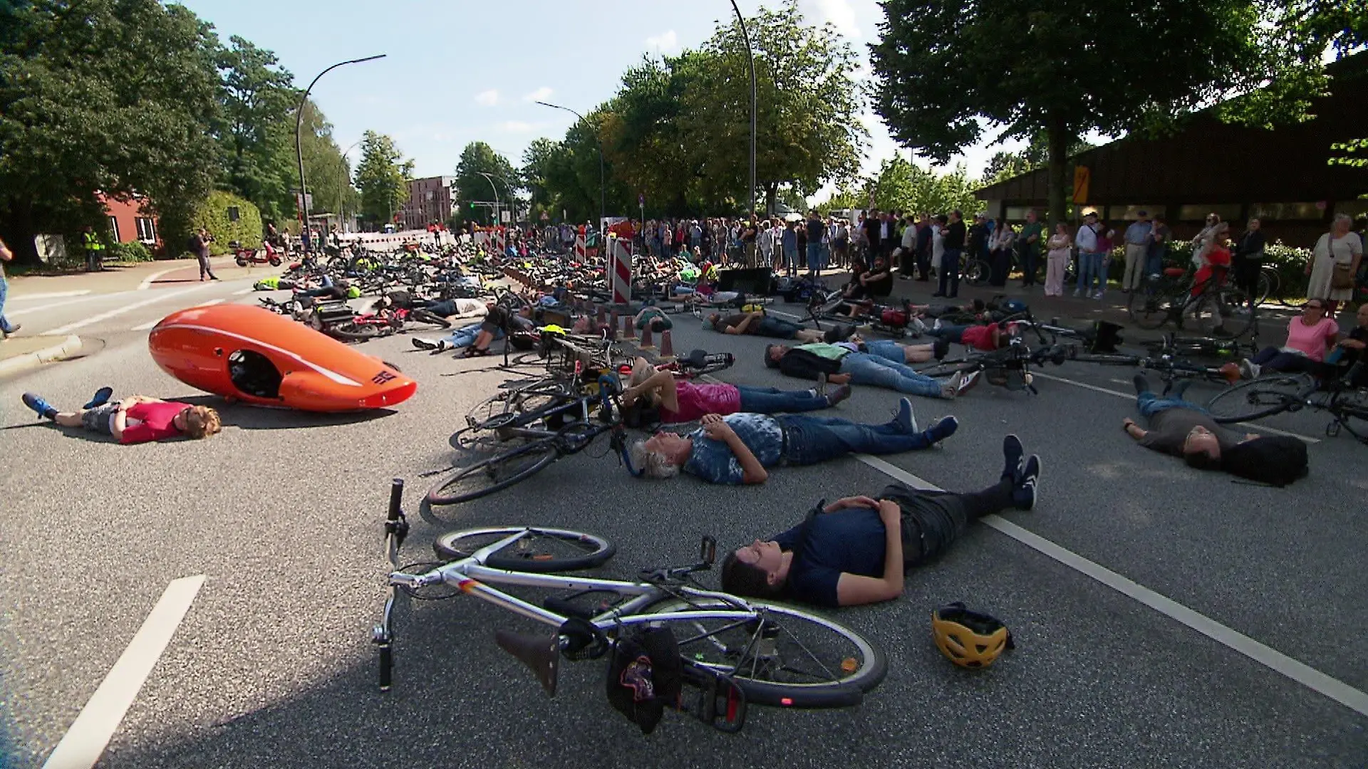 Auf einer abgesperrten Straße legen sich Menschen in einer Protestaktion auf die Straße.