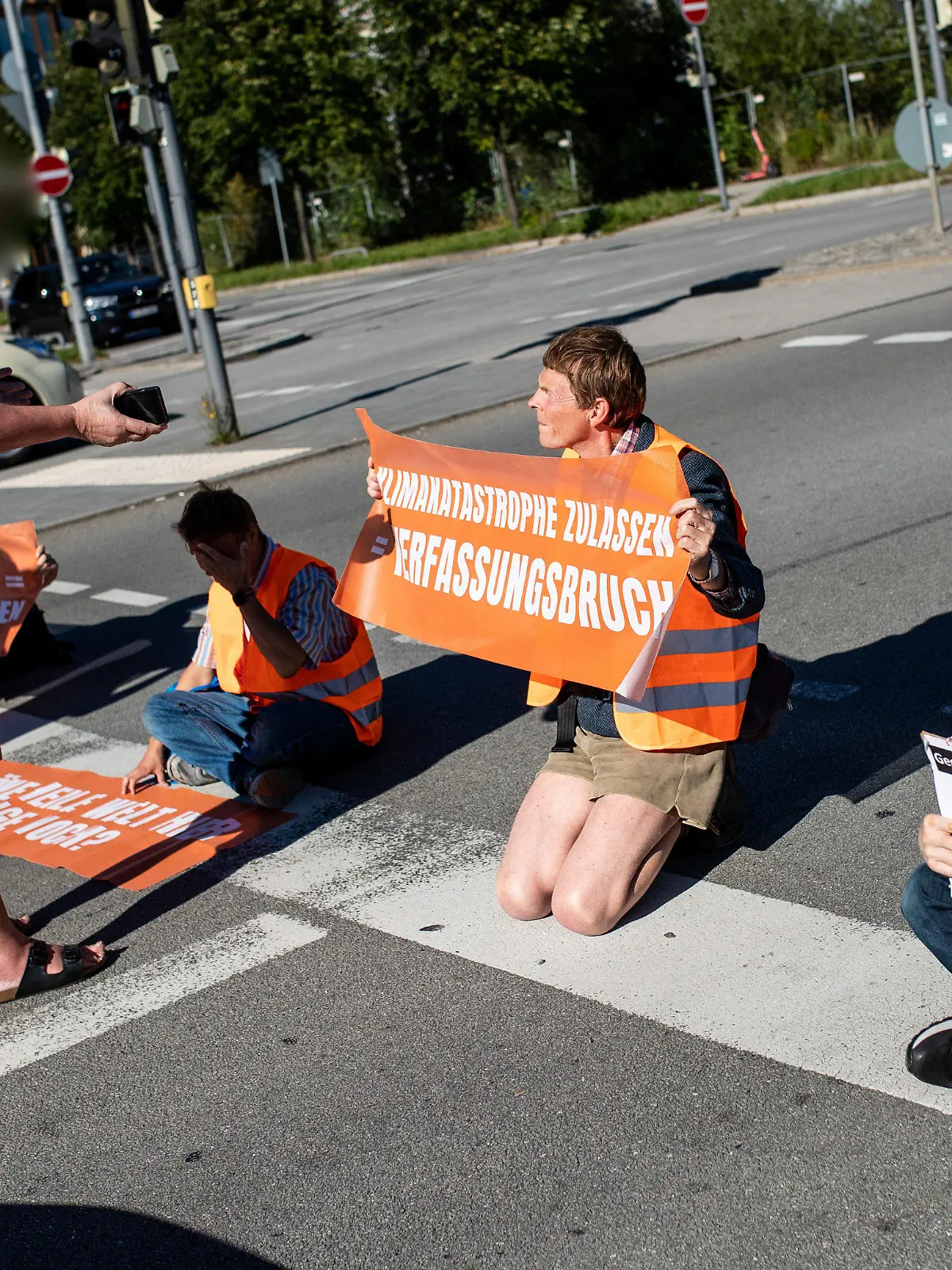 04.09.2023, Bayern, München: Klimaaktivisten der ·"Letzten Generation"· bilden eine Straßenblockade und werden von einem Autofahrer beschimpft. Die Aktion richtet sich gegen die IAA. Die Internationale Automobil-Ausstellung IAA MOBILITY 2023 findet in München von 05.-10. September statt. Foto: Christoph Schmidt/dpa +++ dpa-Bildfunk +++