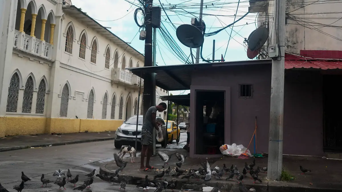 A man feeds pigeons on a street where Gilberto Hernandez, a member of Panama's national soccer team, was shot and killed in Colon, Panama, Monday, Sept. 4, 2023. Hernández was the second member of the national team killed in Colon in the past six years. (AP Photo/Arnulfo Franco)