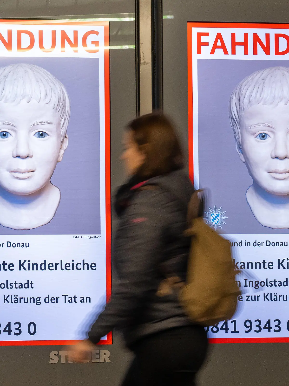 ARCHIV - 05.01.2023, Bayern, München: Eine Frau geht am Ostbahnhof an einem digitalen Fahndungsplakat vorbei. Vor mehr als einem Jahr entdeckt ein Kanufahrer eine Kinderleiche in der Donau. Wer der Junge war und was hinter der Tat steckt, ist bis heute nicht geklärt. Nach einem Aufruf der Polizeibehörde Interpol gibt es nun Hinweise. (zu dpa: «Interpol erhält nach Aufruf etliche Hinweise zu totem Jungen in Donau») Foto: Peter Kneffel/dpa +++ dpa-Bildfunk +++