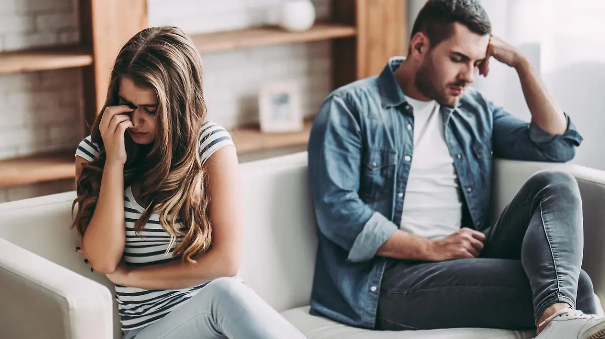 Upset couple at home. Handsome man and beautiful young woman are having quarrel. Sitting on sofa together. Family problems.