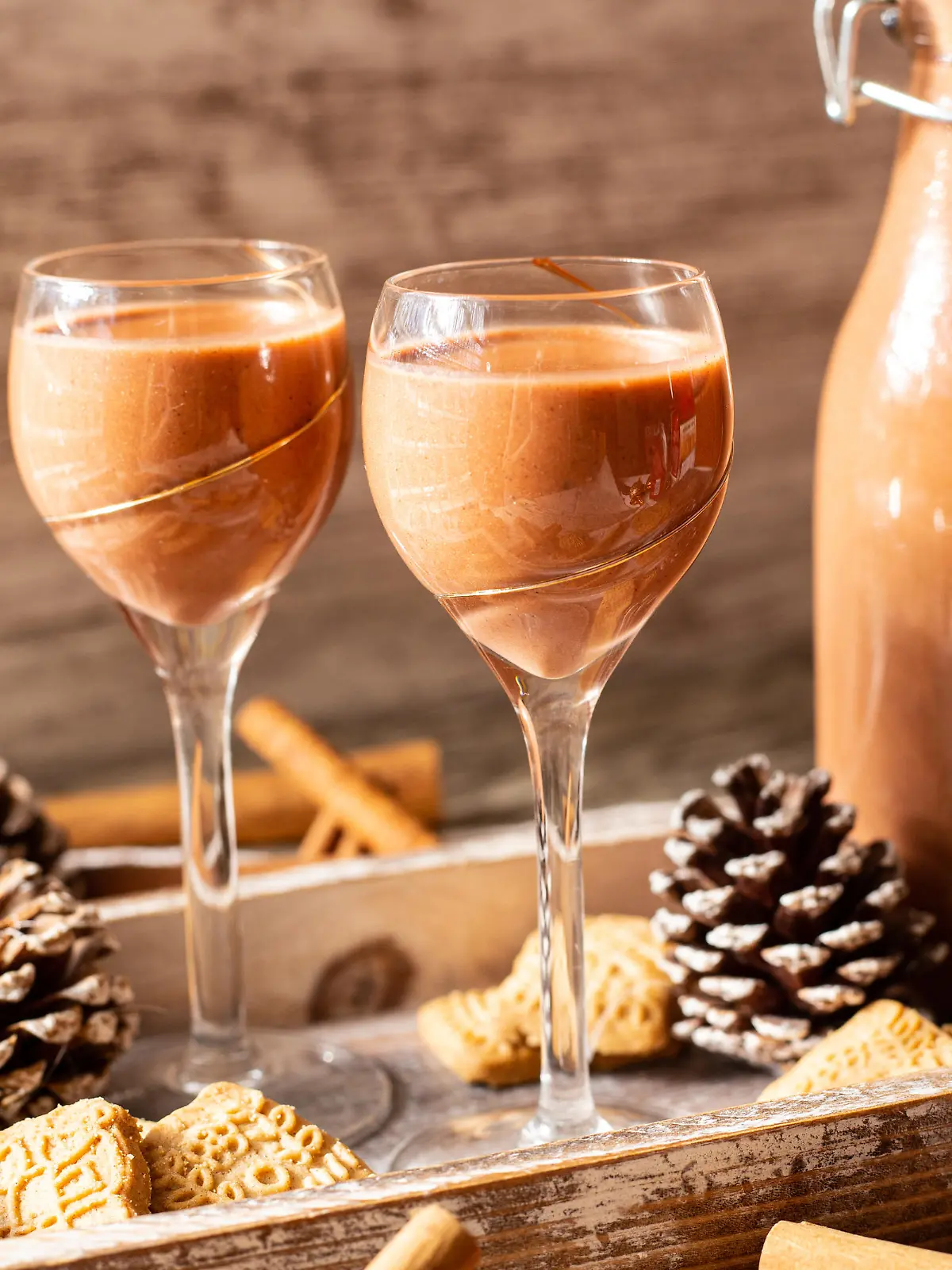 Liqueur in a bottle decorated with pine cones an spekulatius. Part of a series. Liqueur in glass, bottle standing besides. Cinnamon sticks