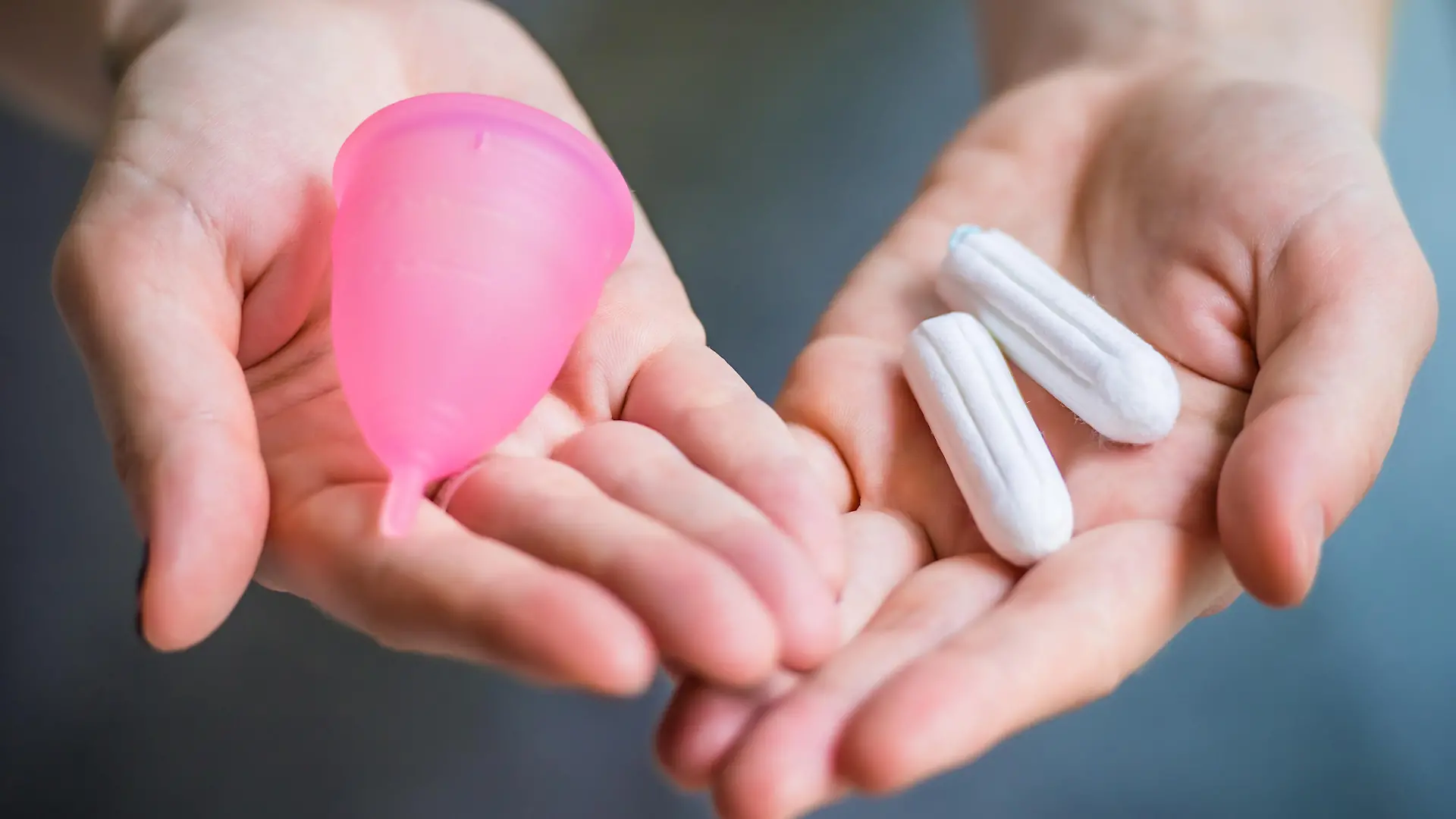 Young woman hands holding different types of feminine hygiene products - menstrual cup and tampons