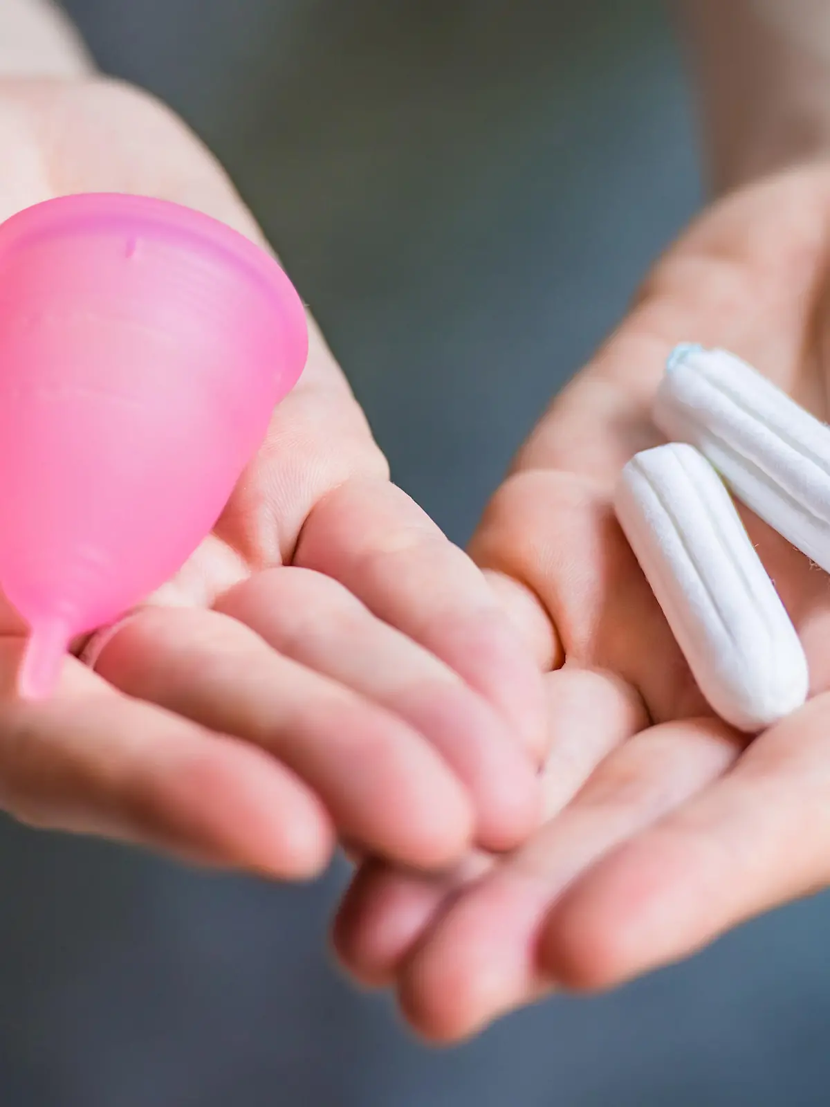 Young woman hands holding different types of feminine hygiene products - menstrual cup and tampons