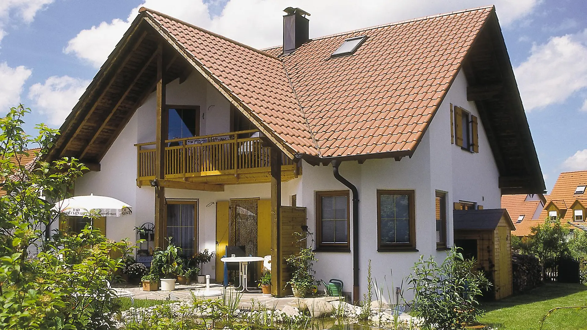 Ein Einfamilienhaus mit Terrasse und Teich.