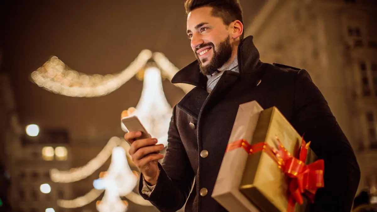 Young man holding Christmas gifts. Checking his smart phone. Wearing warm clothing. Vienna, Austria.