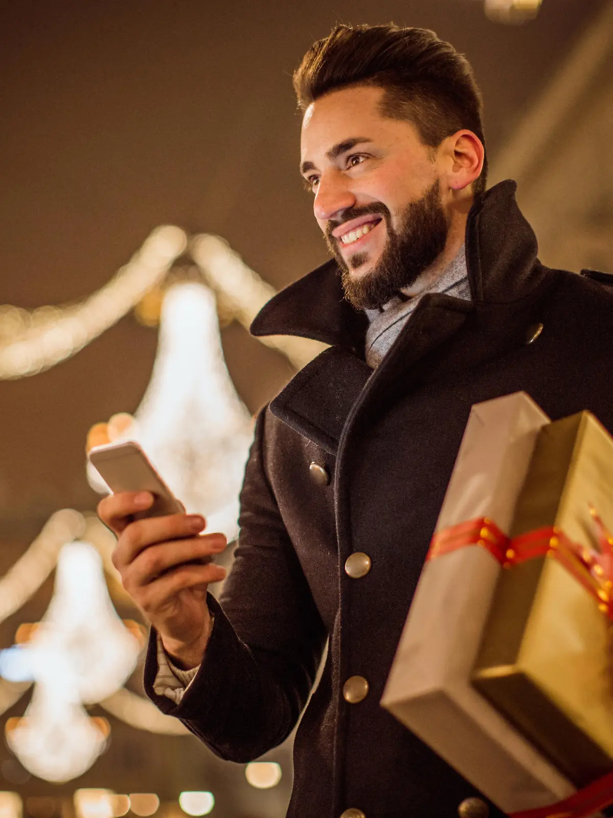 Young man holding Christmas gifts. Checking his smart phone. Wearing warm clothing. Vienna, Austria.