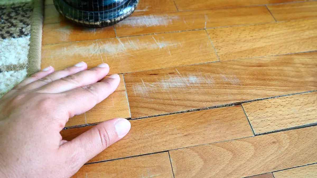 Scratched old parquet flooring needs maintenance. The parquet is damaged by scratches from prolonged use. Master's hands show damage to the floor. The leg of an antique wooden bed.