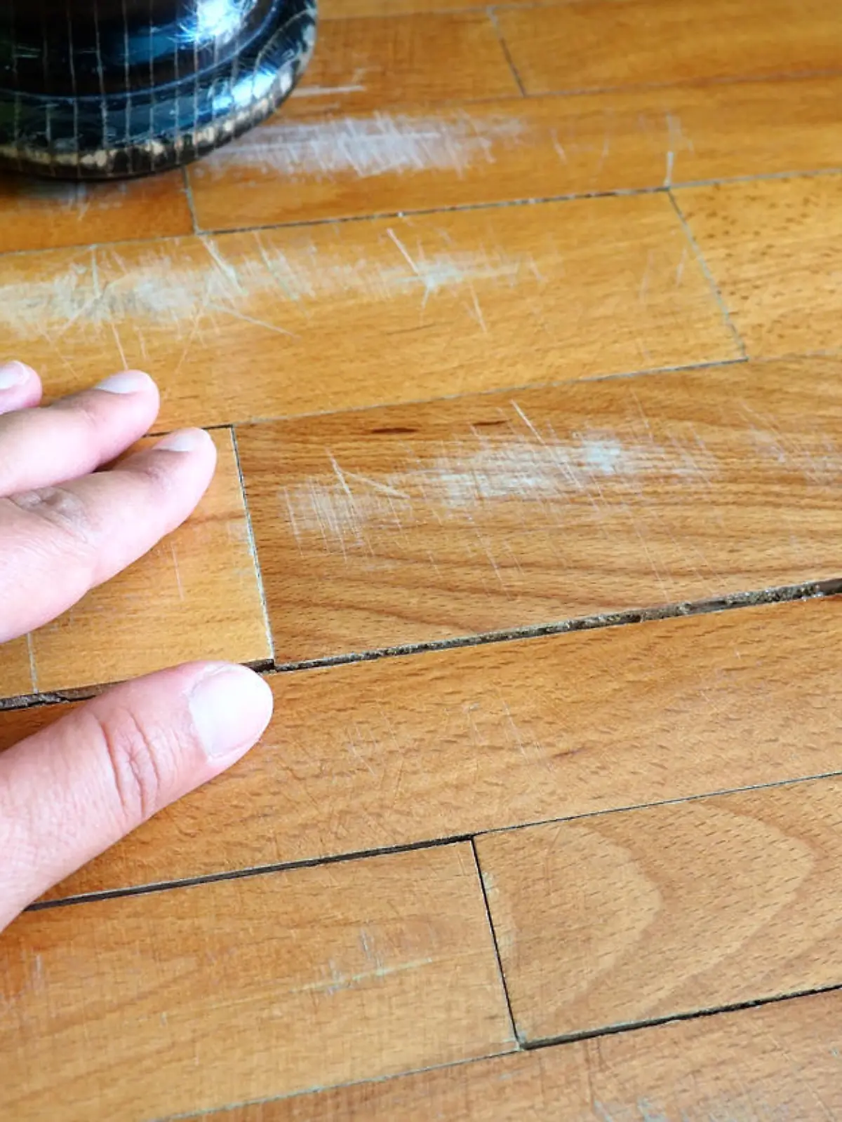 Scratched old parquet flooring needs maintenance. The parquet is damaged by scratches from prolonged use. Master's hands show damage to the floor. The leg of an antique wooden bed.